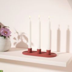 three candles are on a red stand next to a vase with purple flowers in it