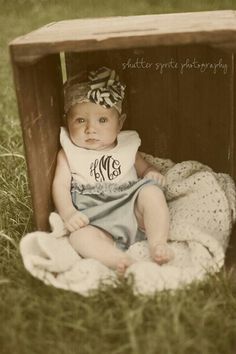 an old photo of a baby sitting in a crate on the grass with a blanket