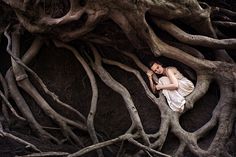 a woman is sitting in the roots of a tree