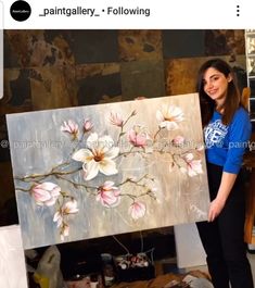 a woman standing in front of a painting holding a large piece of art with flowers painted on it