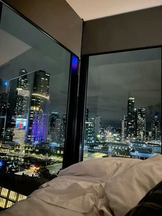 a bed sitting next to a window with city lights in the backgroung