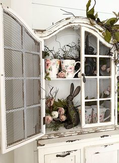 an old china cabinet with flowers and plants on it's doors is decorated in white