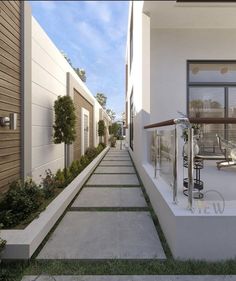 an empty walkway between two buildings with plants on each side and another building in the background