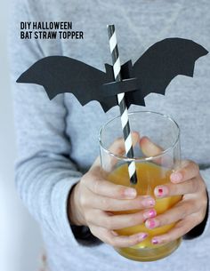 a woman holding a glass with a bat straw topper on it