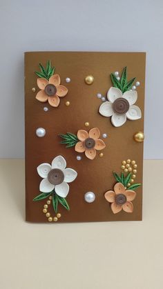 a brown card with flowers and pearls on the front, sitting on a table next to a white wall