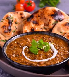 some food is in a black bowl on a plate with pita bread and tomatoes