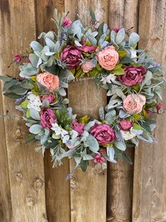 a wreath with pink flowers and greenery hanging on a wooden fence, ready to be hung