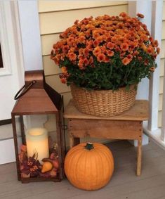 a basket full of flowers sitting next to a lantern and pumpkin on the front porch