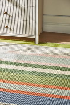 a multicolored striped rug in front of a dresser