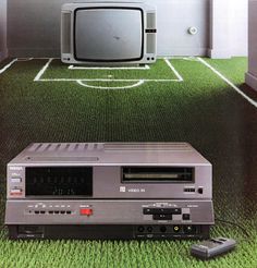 an old tv sitting on top of a green carpeted floor next to a remote control