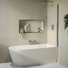 a white bath tub sitting next to a mirror and potted plant in a bathroom