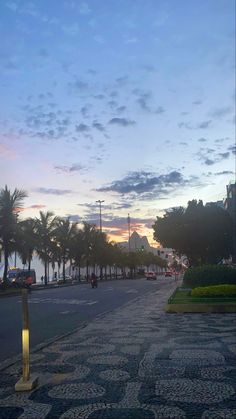 an empty street with palm trees on both sides and the sun setting in the distance