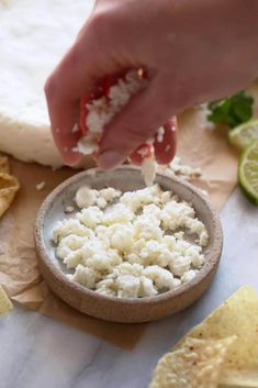 someone is dipping cheese into a bowl with tortilla chips and lime wedges