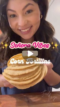 a woman holding up a stack of tortillas