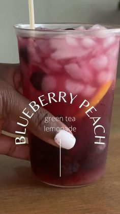 a hand holding a cup with blueberry peach tea in it