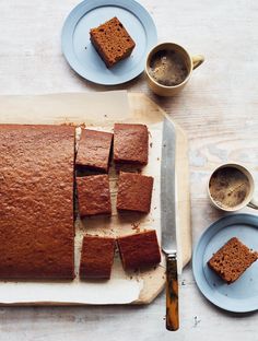 slices of cake sitting on top of a cutting board next to cups and saucers