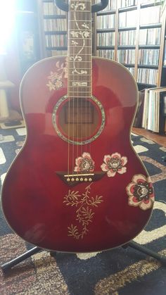 a red guitar sitting on top of a stand in front of a book shelf filled with books