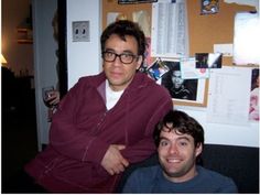 two men sitting next to each other in front of a refrigerator