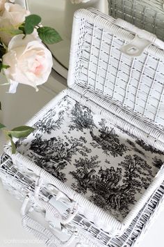 a white wicker box sitting on top of a table next to a vase with flowers