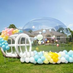 an inflatable bubble filled with balloons on top of a lush green field next to a house