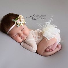 a newborn baby is sleeping on her side wearing a headband with flowers in it's hair