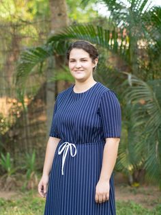 a woman in a blue dress is smiling at the camera with palm trees behind her