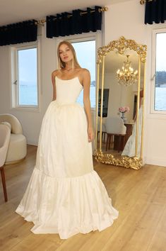 a woman standing in front of a mirror wearing a white dress with tiered ruffles