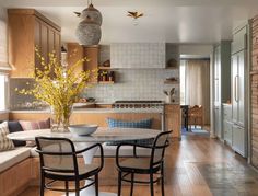 a dining room table with chairs and a bench in front of the kitchen counter area