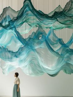 a woman standing in front of a sculpture made out of blue and white wavy material