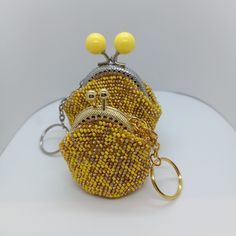 a small purse with yellow beading and two metal rings on the front, sitting on a white surface