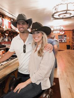 a man and woman in cowboy hats are posing for a photo at the bar with their arms around each other