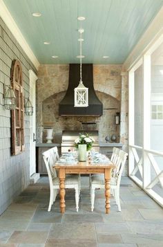 an outdoor kitchen and dining area with stone walls, tile flooring and white chairs