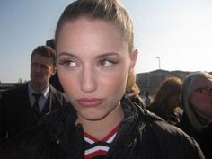 a woman in a black jacket and red striped shirt is looking at the camera with other people behind her