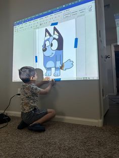 a young boy sitting on the floor in front of a projector screen with a cartoon cat drawn on it