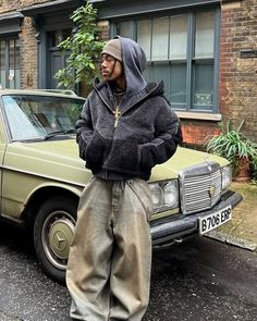 a man standing next to a car in front of a building with a hood on