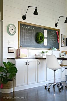 a kitchen with white cabinets and a chalkboard on the wall above it, along with a potted plant