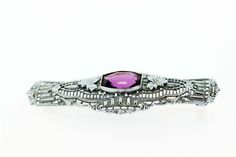 This brooch is made in 10K white gold and has beautiful engraved detail and filigree. In the center is a bezel set amethyst that has milgrain accents around it, with detailed engraved leaves on either side.The brooch measures 49.42mm wide, 18.42mm long, and 5.13mm tall. --Please reference our policy for more details-- For International orders, please provide a phone number for shipping purposes. Just place a note in the comment box during check out.Thank you.** C8830 GVVC Elegant Amethyst Brooches For Wedding, Elegant Purple Brooches For Anniversary, Heirloom Filigree Brooches For Formal Occasions, Antique Purple Brooches For Formal Occasions, Antique Purple Formal Brooches, Classic Purple Filigree Jewelry, Elegant Purple Gemstone Brooches, Purple Filigree Formal Jewelry, Purple Filigree Jewelry For Formal Occasions