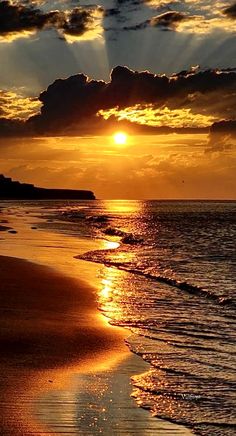 the sun is setting over the ocean with clouds in the sky and sand on the beach