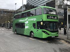 a green double decker bus parked on the side of the road in front of a tall building