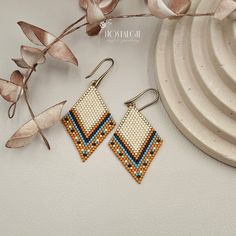 a pair of beaded earrings sitting on top of a white plate next to a plant