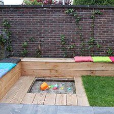 a wooden bench sitting on top of a lush green field next to a brick wall