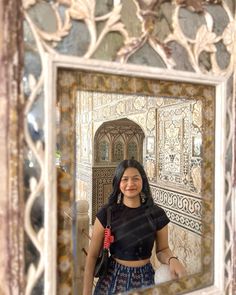 a woman standing in front of a mirror with an ornate design on the wall behind her