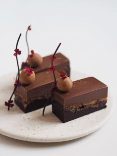 three pieces of chocolate dessert on a white plate with red flowers and small cherries