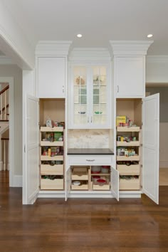 a kitchen with white cupboards and wooden flooring in front of an open pantry