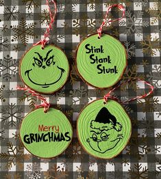 three green christmas ornaments with funny faces and words on them, hanging from red ribbon