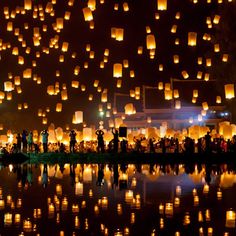 many people are flying lanterns in the air over water at night with lights reflecting on the water