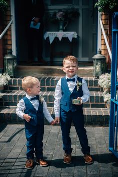 two young boys in blue vests and bow ties standing on steps with their arms around each other