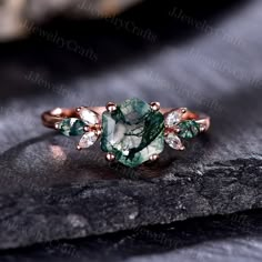 a green and white diamond ring sitting on top of a black stone slab with leaves around it