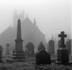 a cemetery with many headstones in front of an old church on a foggy day