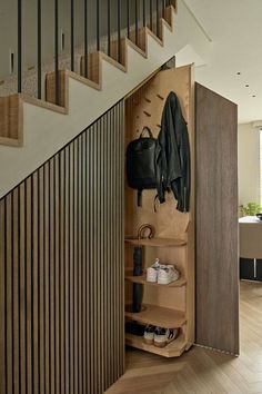 an open closet with shoes and coat hanging on the wall next to a stair case